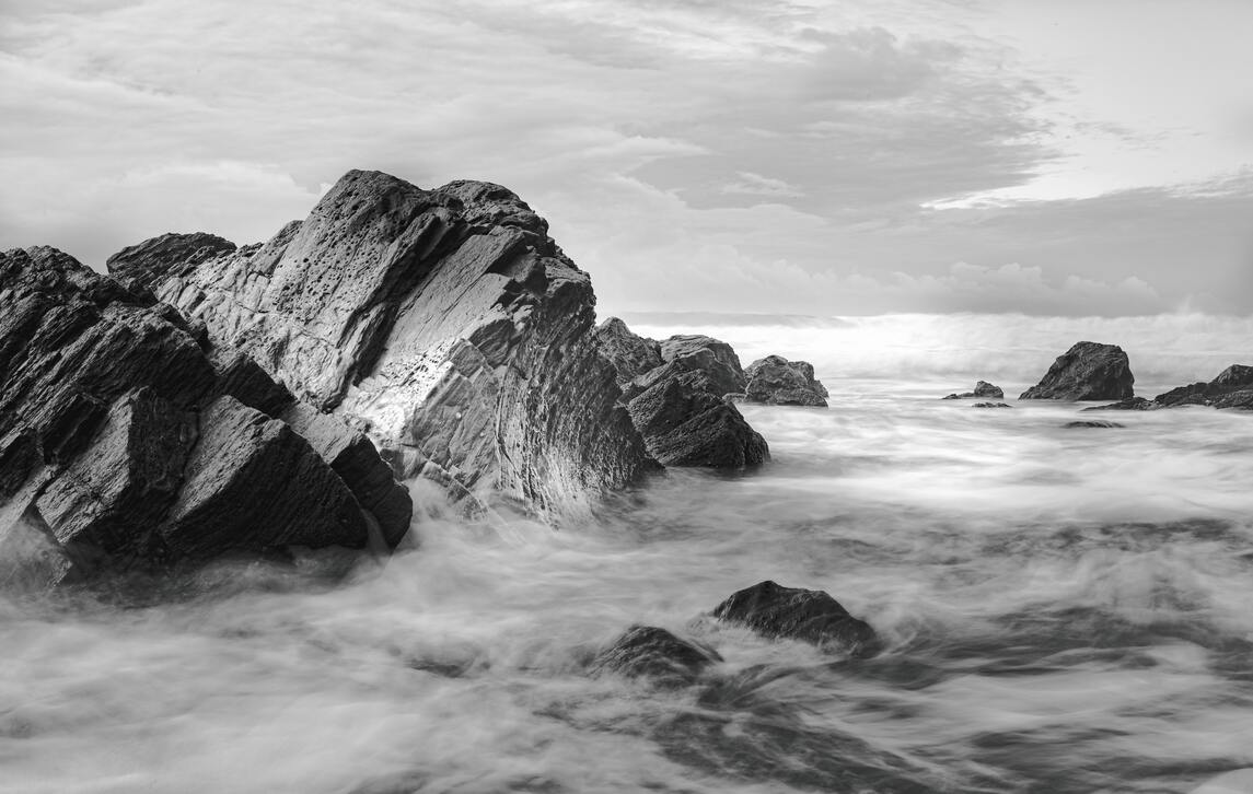 cached/dharmx_walls/monochrome/a_rocky_beach_with_waves_crashing_onto_rocks.jpg